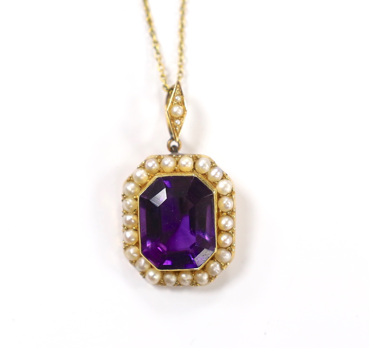 An Edwardian 15ct, amethyst and seed pearl cluster set pendant, overall 33mm, on a 9ct chain, 70cm, chain, 2.5 grams.
